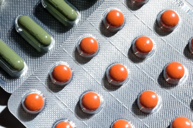 Le pillole arancioni e verdi in un blister di alluminio giacciono su uno sfondo chiaro. grande iplano. vista dall'alto