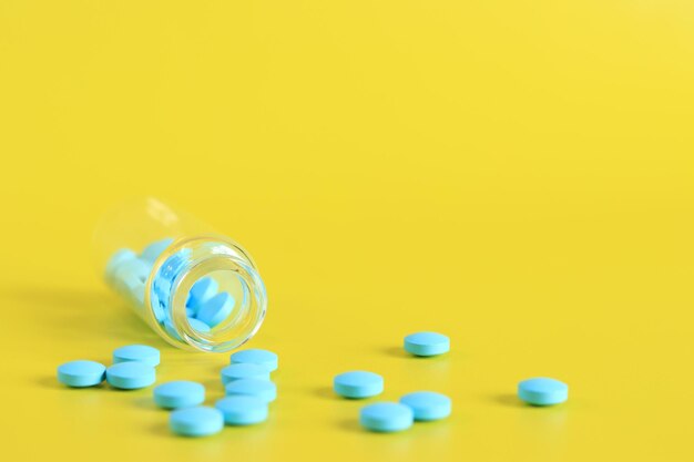 Le pillole blu vengono versate da una bottiglia di vetro su uno sfondo giallo integratori alimentari