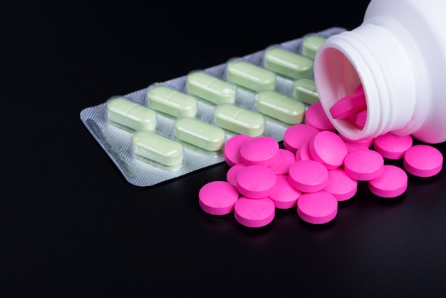 Le pillole sono rosa e vesciche con pillole verdi su fondo nero.