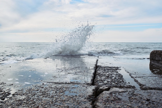 Le potenti onde del mare si infrangono sul frangiflutti di pietra durante la tempesta e gli schizzi volano in diverse direzioni