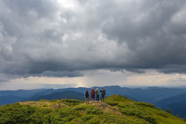 Le quattro persone attive in piedi sulla montagna contro bellissime nuvole