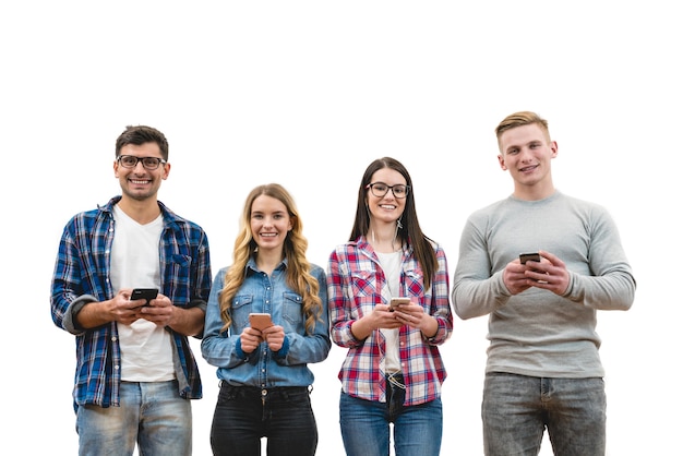 Le quattro persone felici con i telefoni stanno sullo sfondo del muro bianco