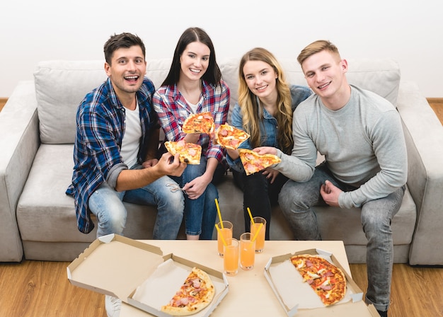 Le quattro persone felici sul divano che mangiano la pizza