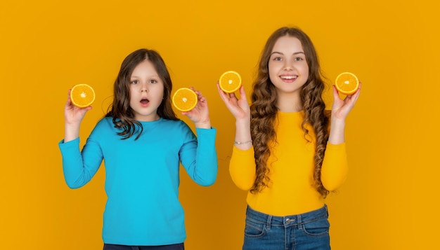 Le ragazze adolescenti stupite tengono la frutta arancione su sfondo giallo