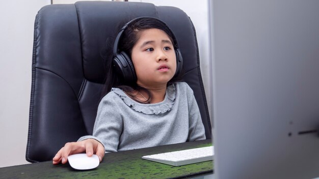 Le ragazze asiatiche studiano online con i laptop. I bambini indossano le cuffie per la digitazione del taccuino della tastiera che imparano utilizzando lezioni su Internet in quarantena. Gli studenti imparano con la lezione online su Internet dalla scuola Covid-19