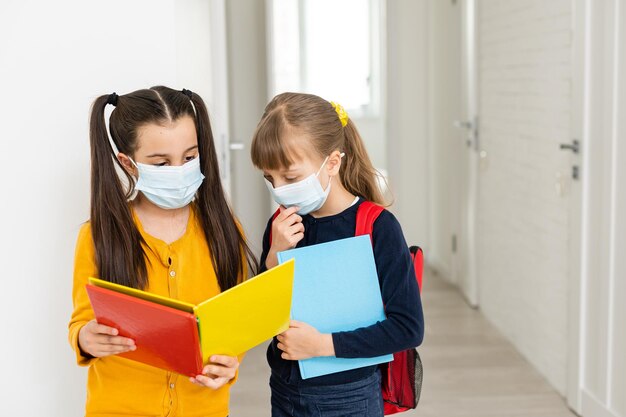 Le ragazze carine delle primarie si abbracciano con la maschera. Le ragazze della scuola portano i quaderni in mano e si salutano prima di entrare a scuola.