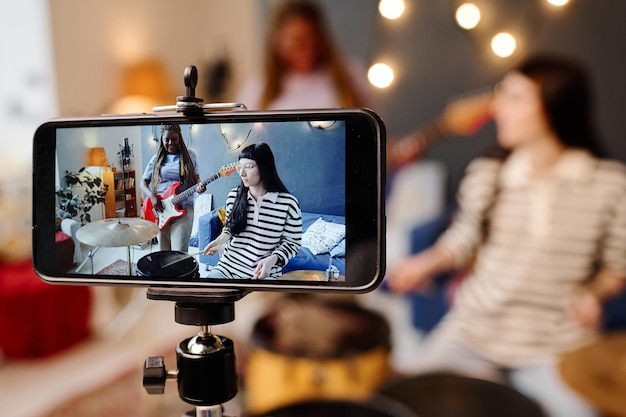 Le ragazze registrano la loro performance sullo smartphone suonando la chitarra e la batteria in studio