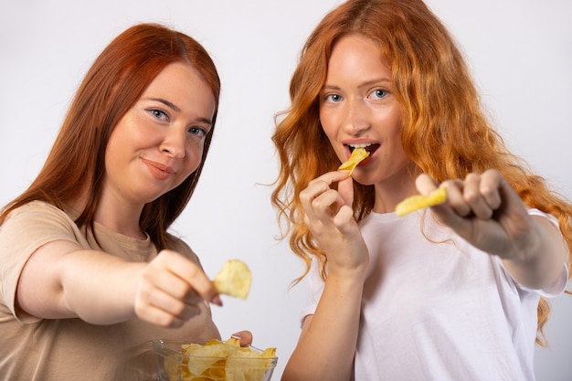 Le ragazze rosse stanno mangiando patatine fritte e in posa isolata