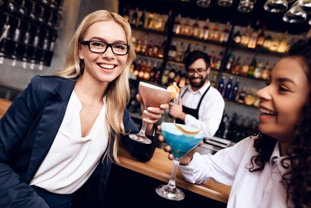 Le ragazze sono seduti al bar con cocktail.