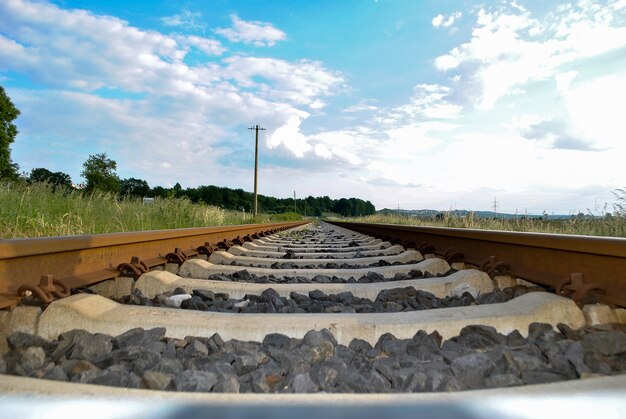 Le rotaie ferroviarie e le traversine hanno sparato in basso sopra il primo piano del suolo su uno sfondo di cielo nuvoloso