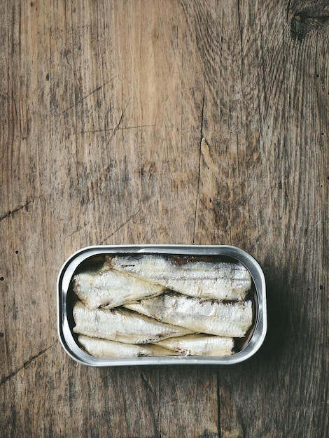 Le sardine aperte possono sul vecchio tavolo da cucina in legno, vista dall'alto