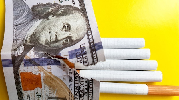 Le sigarette classiche stanno su banconote da cento dollari USA. Sigarette su una banconota da cento dollari su uno sfondo giallo.
