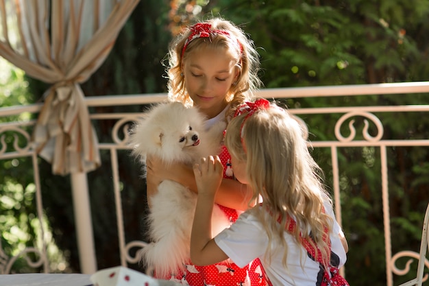 Le sorelle abbracciano il loro cane con amore. Bellissimi bambini biondi giocano con un piccolo cane.