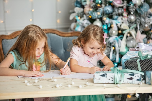 Le sorelline delle bambine con i regali belli nell'interno di Natale scrivono una lettera a Babbo Natale