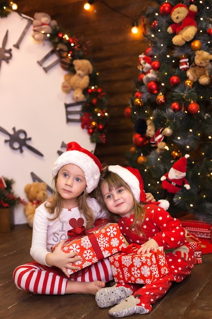 Le sorelline in pigiama rosso decorano l'albero di Natale e aprono i regali in soggiorno