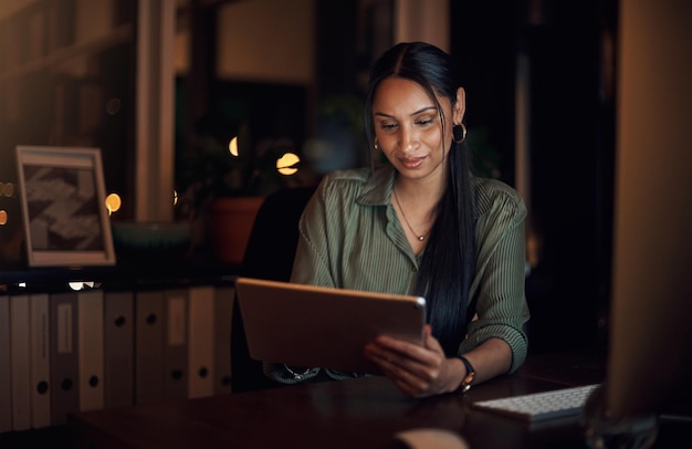 Le sue connessioni wireless sono tutto ciò di cui ha bisogno per rispettare la scadenza Inquadratura di una giovane donna d'affari che usa un tablet digitale in un ufficio di notte