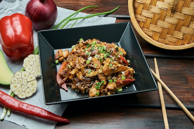 Le tagliatelle di cellophane con mais, peperone dolce, cipolle, carote e pollo fritti su un wok con salsa teriyaki in banda nera sopra. Gustoso cibo di strada asiatico