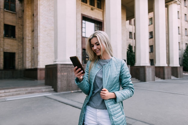 Le telecomunicazioni nella vita di città. Ragazza con gadget, comunicazione moderna, giovane bionda con cellulare in strada