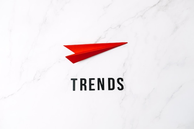 Le tendenze del mondo globale superano le nuove tendenze che prevedono le tendenze delle parole e l'aereo di carta rosso su sfondo rosso