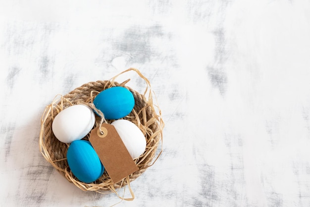 Le uova di Pasqua bianche e blu giacciono su un vassoio fatto di spago sotto di loro c'è il fieno