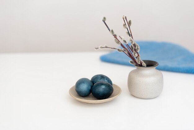 Le uova di Pasqua blu giacciono su un tavolo bianco accanto a un vaso con salice