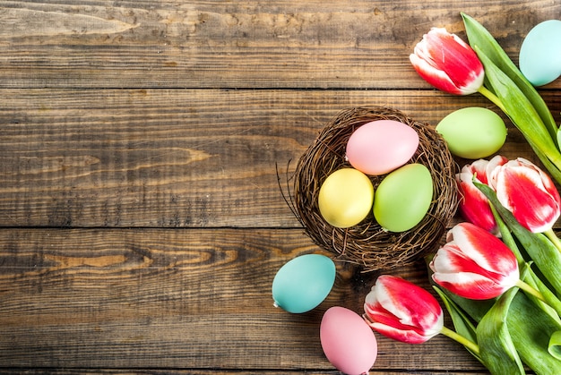 Le uova di Pasqua multicolori con i tulipani fiorisce su fondo di legno, vista superiore dello spazio della copia