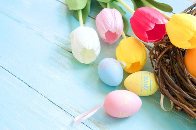 Le uova di Pasqua variopinte in nido con il tulipano fiorisce su fondo di legno blu.