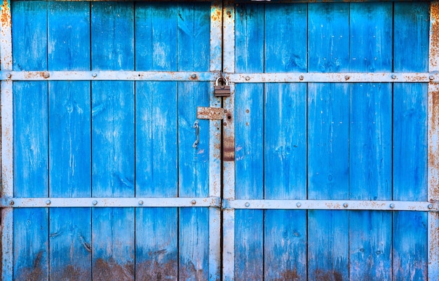 Le vecchie grandi porte in legno dipinte di blu e chiuse sul lucchetto Il cancello blu sulla serratura Primo piano di cancelli in legno per lo sfondo