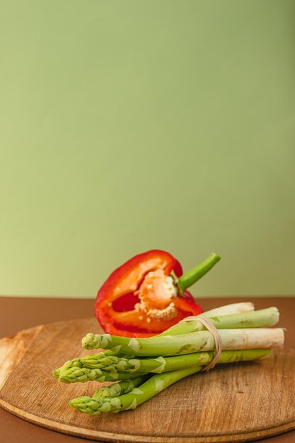 Le verdure giacciono su una tavola di legno asparagi peperoni rossi marrone sfondo verde chiaro posto per il testo