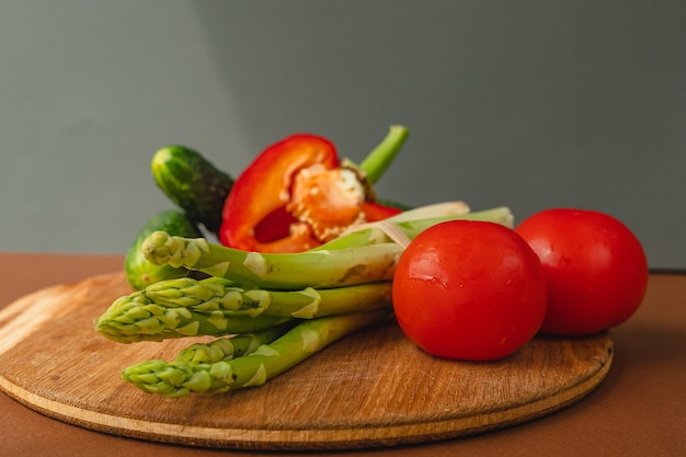 Le verdure giacciono su una tavola di legno pomodori asparagi cetrioli peperoni rossi marrone grigio scuro sfondo posto per il testo