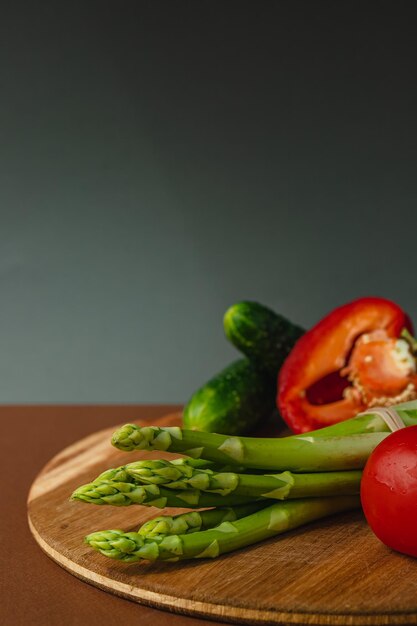 Le verdure giacciono su una tavola di legno pomodori asparagi cetrioli peperoni rossi marrone grigio scuro sfondo posto per il testo