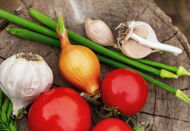 Le verdure si trovano su un fondo di legno, su una cipolla di pomodoro e su un aglio