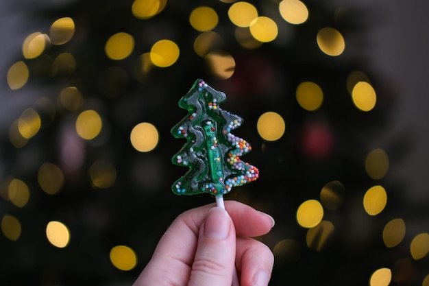 Lecca-lecca a forma di albero di Natale in una mano femminile su uno sfondo di luci sfocate