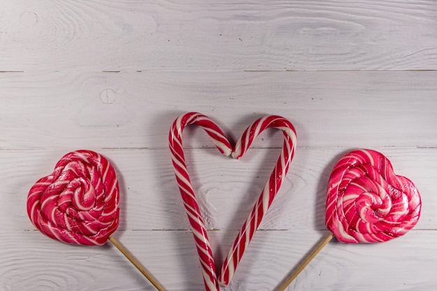 Lecca-lecca e bastoncini di zucchero a forma di cuore su fondo di legno bianco