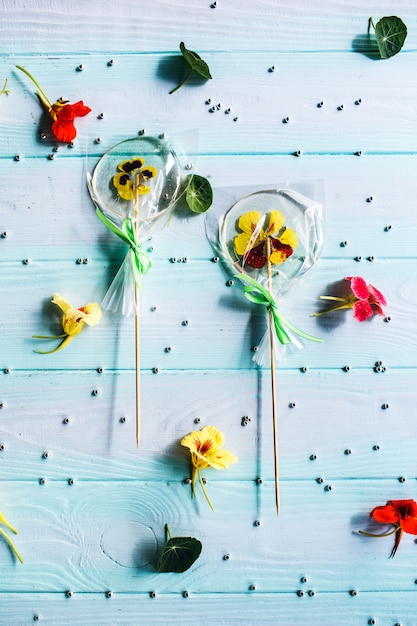 Lecca lecca rotondi piatti fatti a mano con fiori o perline all'interno su una superficie di legno blu. motivo di caramelle, fiori e perle d'argento di pasticceria