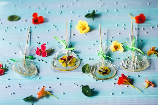 Lecca lecca rotondi piatti fatti a mano con fiori o perline all'interno su una superficie di legno blu. motivo di caramelle, fiori e perle d'argento di pasticceria