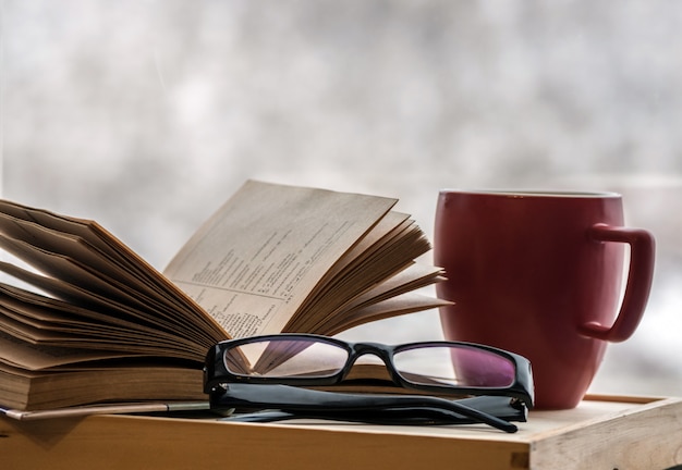 Leggere un vecchio libro con gli occhiali a casa in una fredda sera d'inverno. Leggere un libro a casa con il caffè