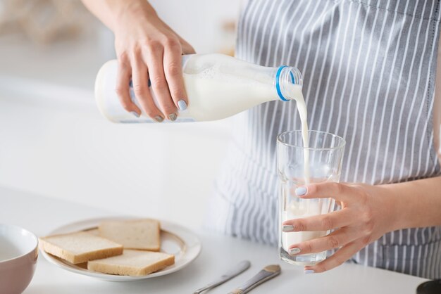 Leggero e fresco. La premurosa giovane madre amorevole prepara una colazione mentre indossa un grembiule e riempie un bicchiere