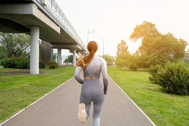 Leggings vestiti da donna e parco estivo su strada asfaltata in esecuzione superiore. Concetto di stile di vita sano. Esercizi femminili attivi e atletici