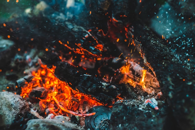 Legna da ardere fumante viva bruciata in primo piano del fuoco. Atmosferico con la fiamma arancione del fuoco. Immagine completa della struttura del falò con le scintille nel bokeh. Caldo vortice di braci ardenti e ceneri nell'aria