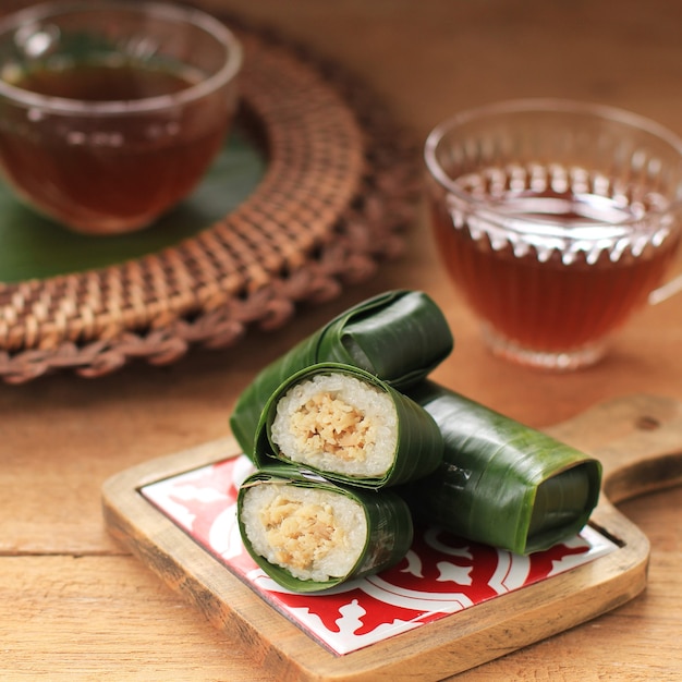 Lemper Ayam servito con tè. Lemper è uno snack indonesiano a base di riso glutinoso ripieno di pollo stagionato a pezzi avvolto in foglie di banana, servito per l'ora del tè