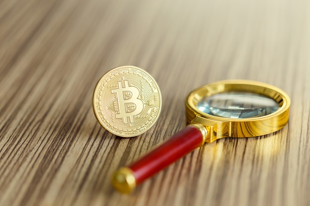 Lente d'ingrandimento con moneta bitcoin dorata