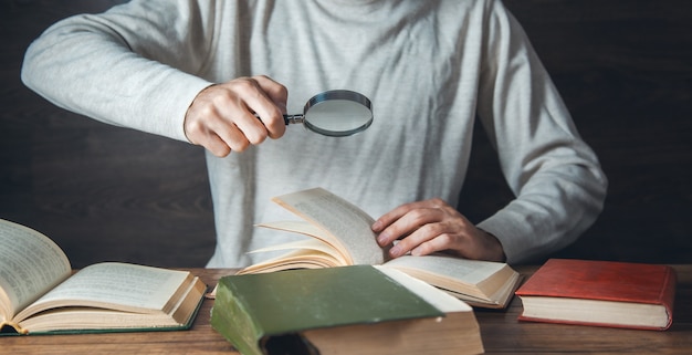 Lente d'ingrandimento della mano dell'uomo e libri sul tavolo