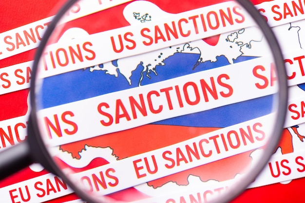 Lente d'ingrandimento in linea con la scritta Sanzioni sulla bandiera della Russia