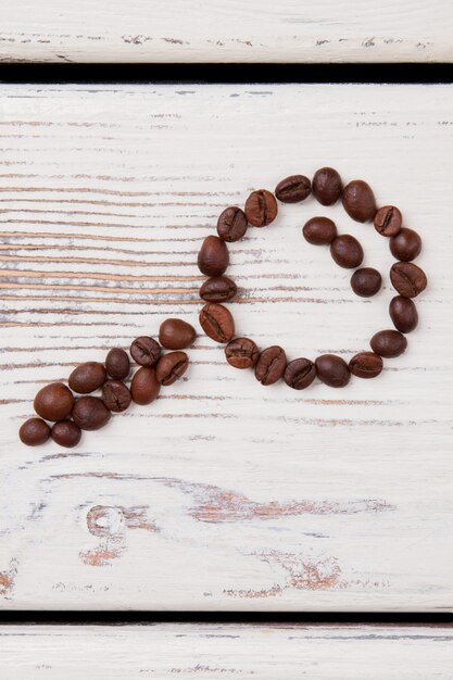 Lente d'ingrandimento in vetro fatta di chicchi di caffè tostati. Il concetto di trovare il caffè. Superficie in legno bianco.