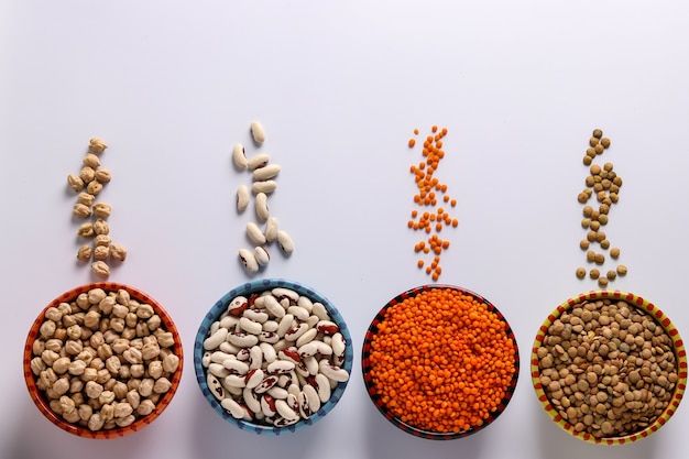 Lenticchie rosse e marroni, ceci e fagioli bianchi sono legumi che contengono molte proteine si trovano su uno sfondo bianco in ciotole, orientamento orizzontale, vista dall'alto