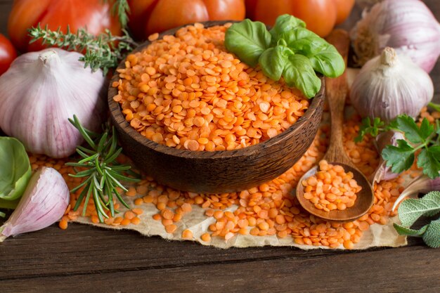 Lenticchie rosse in una ciotola con pomodori, aglio ed erbe aromatiche su legno