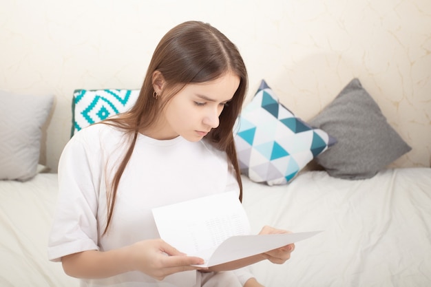 Lettera, avviso. La ragazza legge un foglio di carta a casa, esamina attentamente il testo