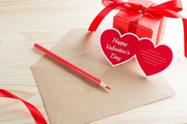 Lettera con cartolina d'auguri a forma di cuore di San Valentino e scatola rossa presente sulla tavola di legno.