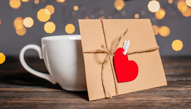 Lettera d'amore con un cuore accanto a una tazza su uno sfondo di luci, amore e concetto di San Valentino su un tavolo di legno